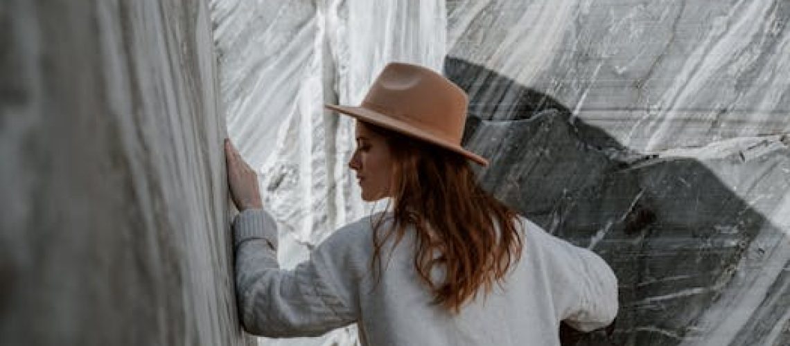 Woman in fedora and sweater exploring rocky marble canyon outdoors.