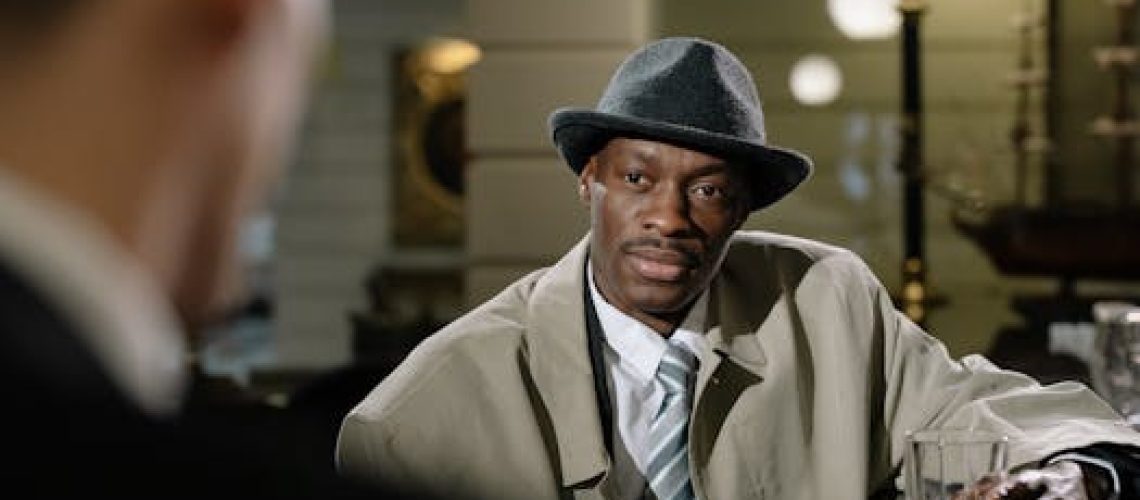 A detective in a trench coat and fedora at a bar, creating a mysterious noir scene.