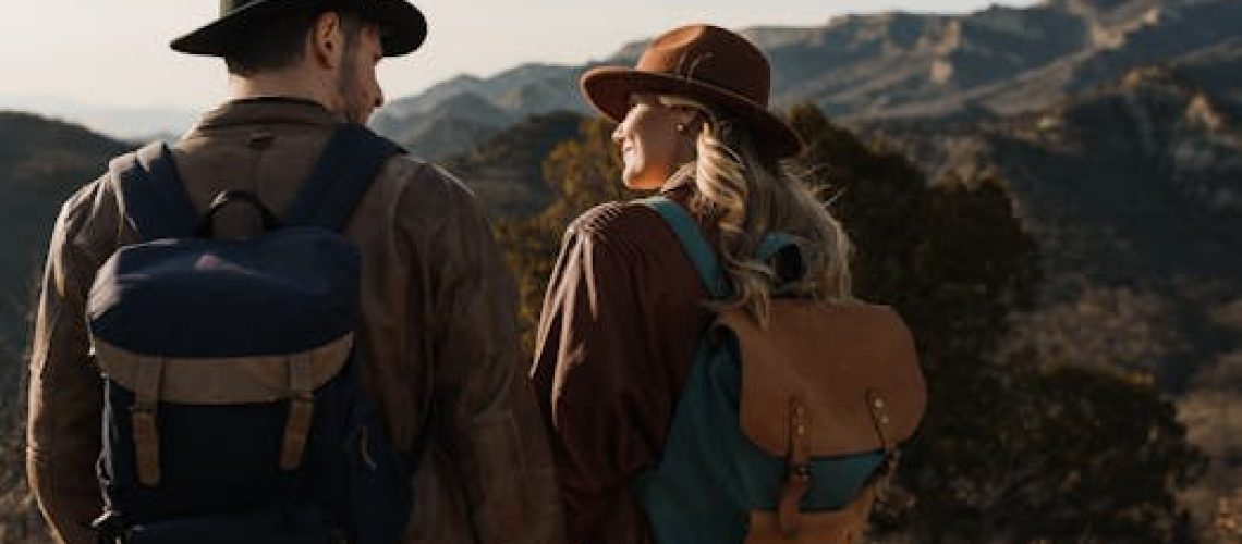 A couple enjoys a mountain hike, wearing hats and backpacks, embracing nature's beauty.